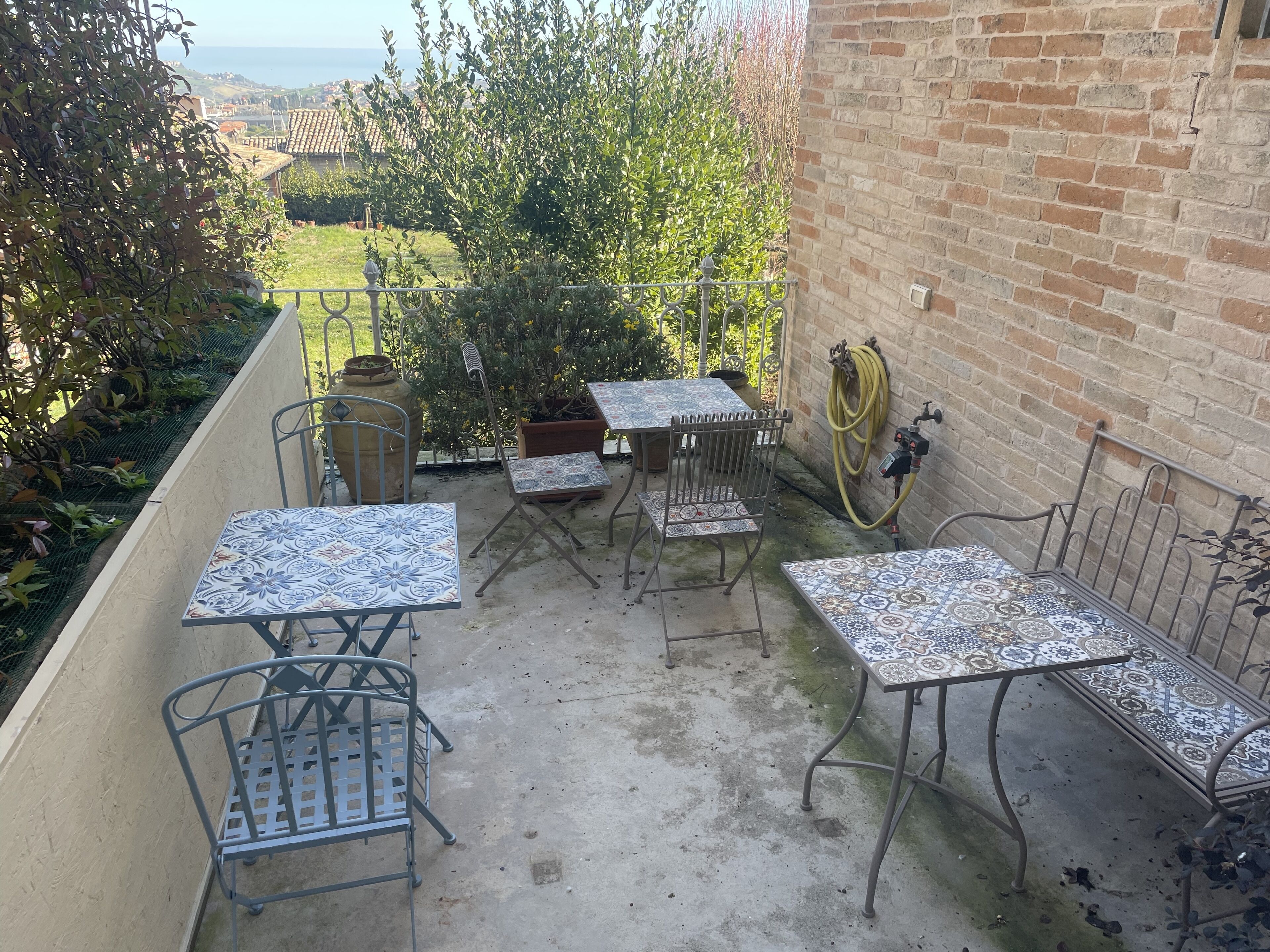 Eine Terrasse im Freien mit Metalltischen und -stühlen, einer Ziegelwand und Meerblick.