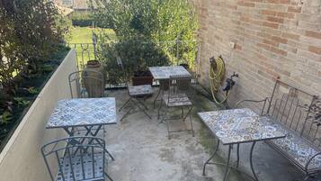 Eine Terrasse im Freien mit Metalltischen und -stühlen, einer Ziegelwand und Meerblick.
