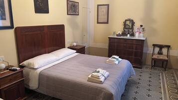 Habitación de hotel con una cama grande, una mesita de noche de madera, un aparador, una silla y un baño con inodoro y lavamanos.