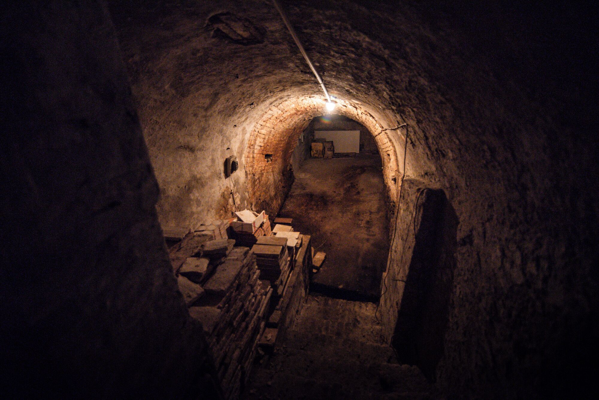 A dimly lit tunnel with a narrow passageway leading to a room with a window.