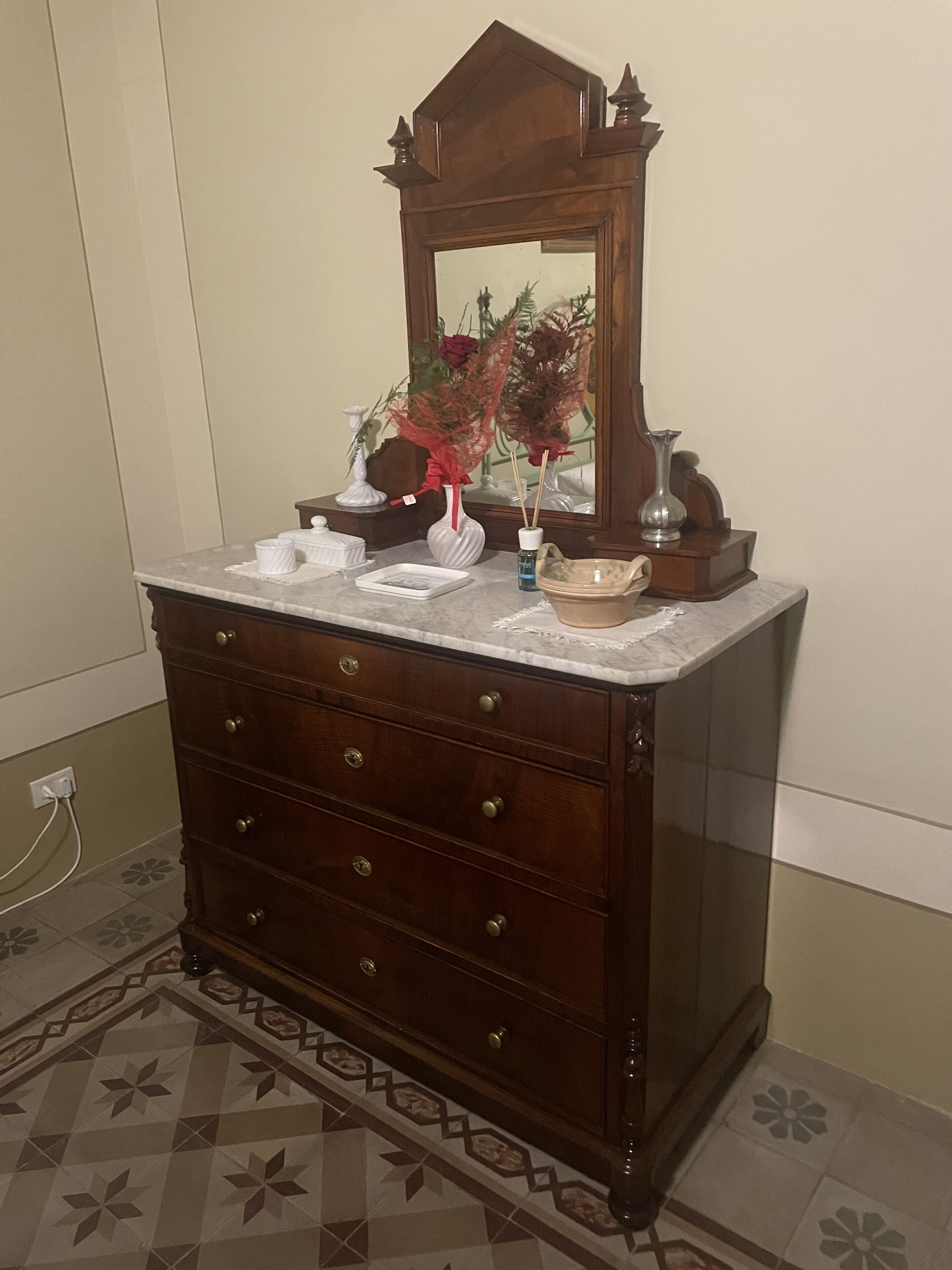 A wooden dresser with a mirror above it, a vase with flowers, and a small decorative item on the dresser.