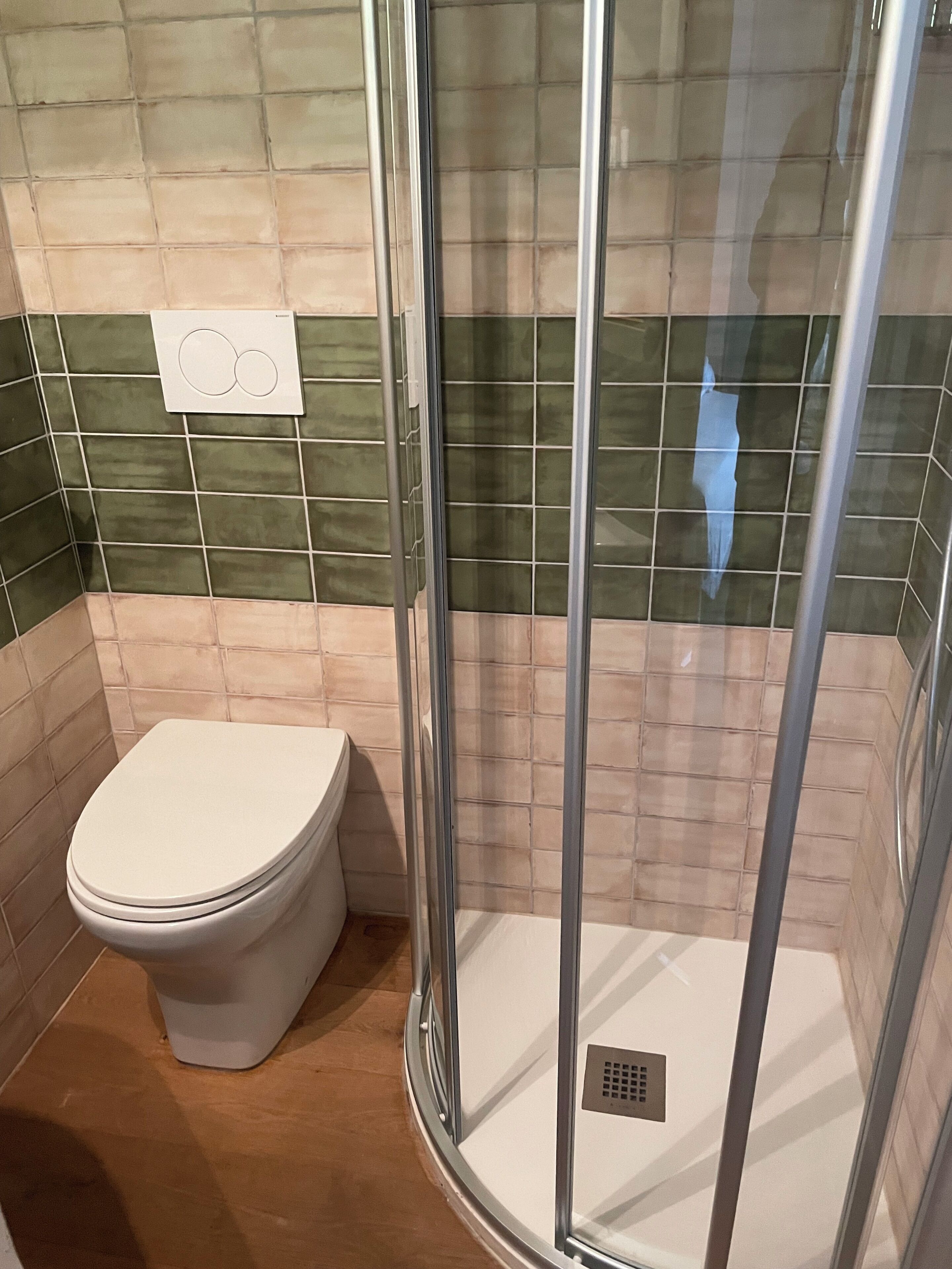 Une salle de bain comprenant des toilettes, un espace douche et un mur carrelé.