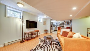 A modern living room with a sofa, a coffee table, and a TV. There is a kitchen in the background with cabinets and a microwave.