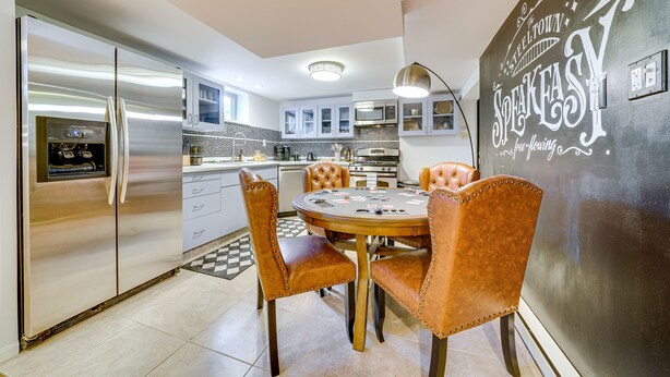A modern kitchen with a stainless steel refrigerator, a dining table with four chairs, and a chalkboard wall with writing.