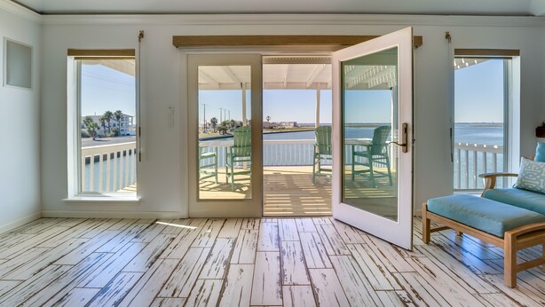 Une pièce spacieuse dotée d’un plancher en bois, d’une porte-fenêtre coulissante donnant sur une terrasse extérieure avec des chaises, et offrant une vue sur l’océan.