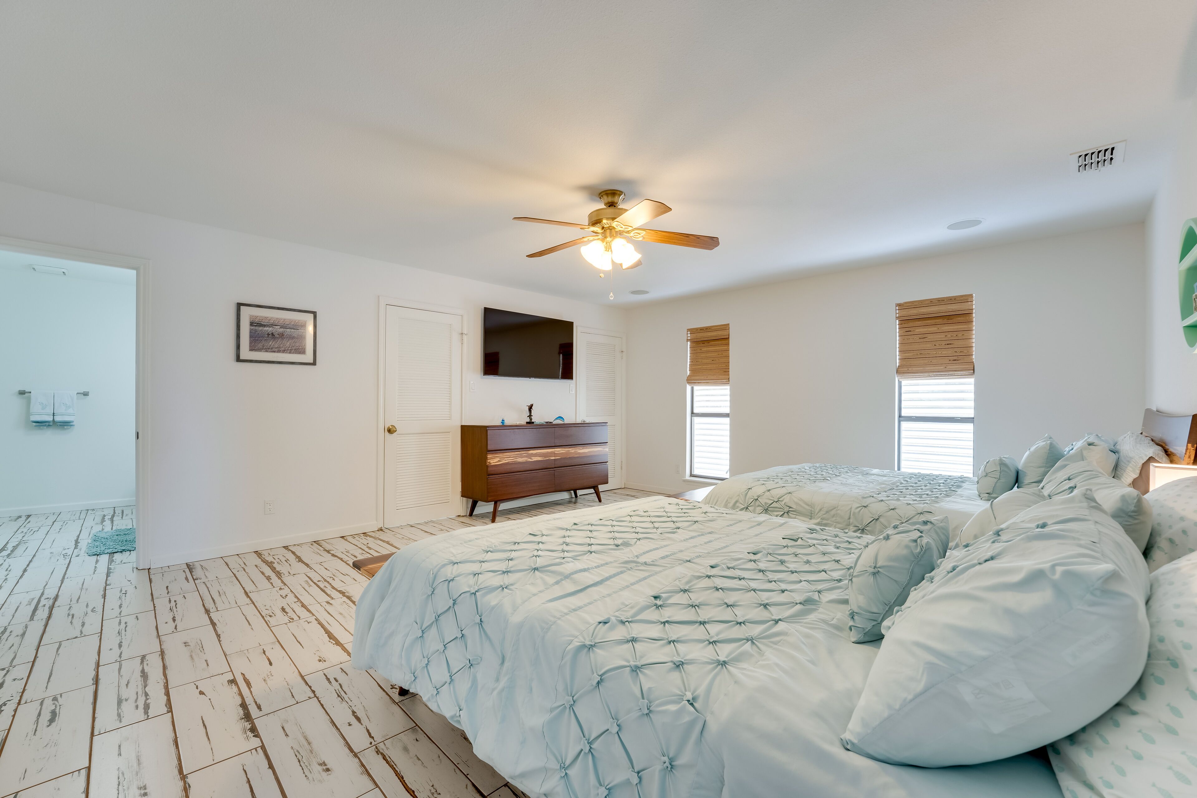 Een slaapkamer met een bed, een dressoir, een plafondventilator en een deur naar een andere kamer.