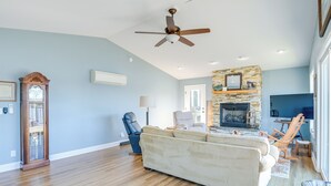 Ein geräumiges Wohnzimmer mit Holzdielen, einem beigefarbenen Sofa, einem blauen Sessel und einem Kamin aus Stein.