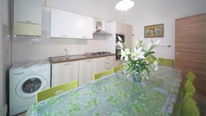 Ett kompakt kök med tvättmaskin, ett matbord med stolar och en vas med blommor.