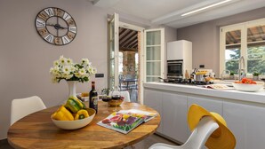 A modern kitchen with a wooden table, a clock, and a vase of flowers. - Villa Dada 10 Emma Villas (Rosignano Marittimo)
