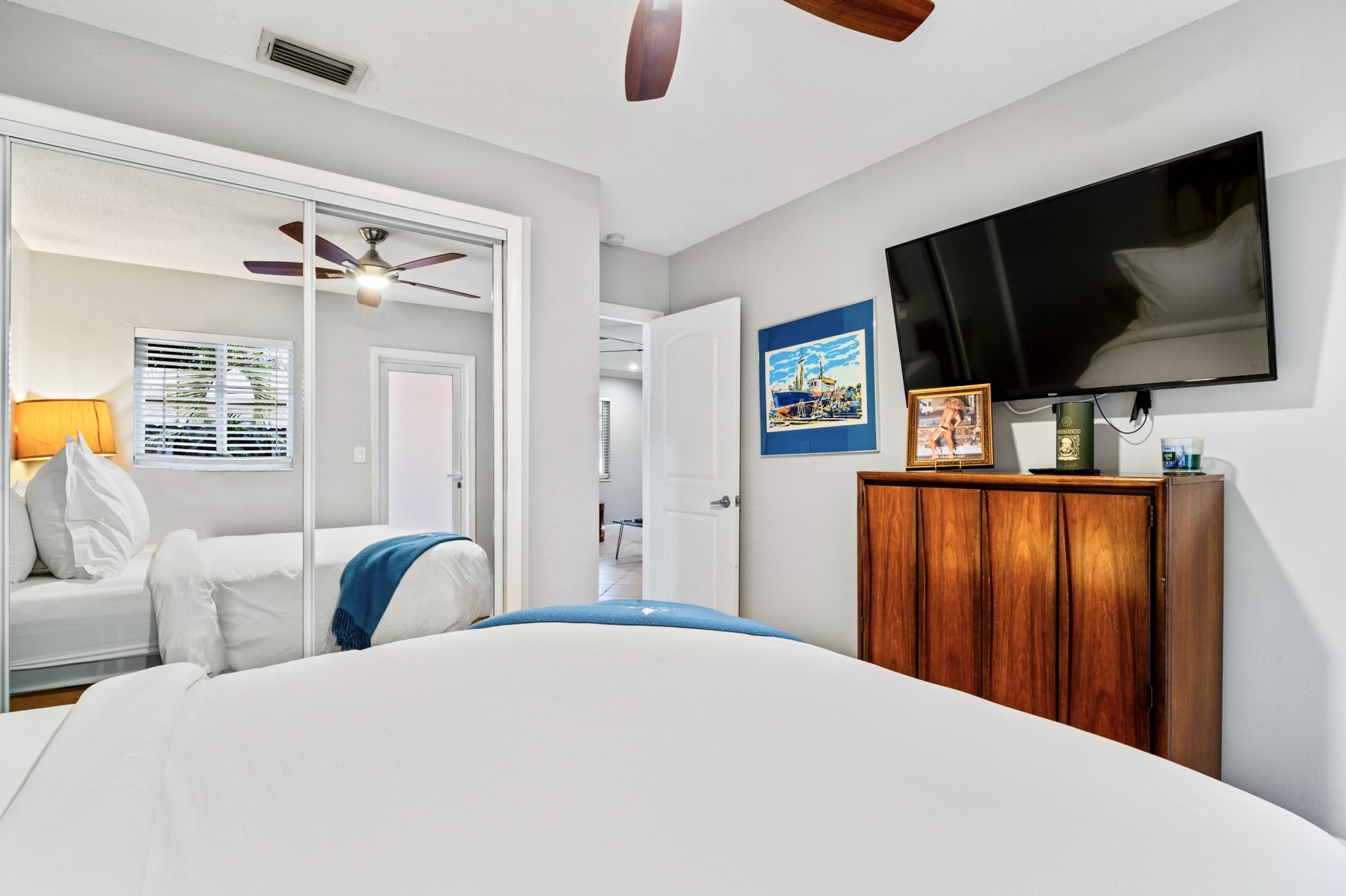 Un dormitorio con cama, televisor, mueble de madera y puerta que da a otra habitación.