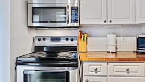 Una cocina con gabinetes blancos, un microondas de acero inoxidable y una estufa.