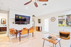 Een moderne woonkamer met een flatscreen televisie, een eethoek met stoelen, een salontafel en een ingebouwde houten kast.