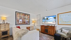 Een woonkamer met een bank, een houten kast, een televisie en een groot, ingelijst schilderij aan de muur.