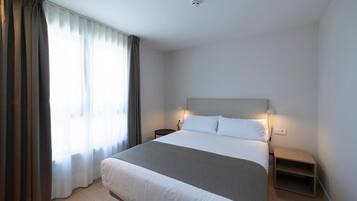 A modern hotel room with a large bed, a bedside table, a nightstand, and a window with curtains.