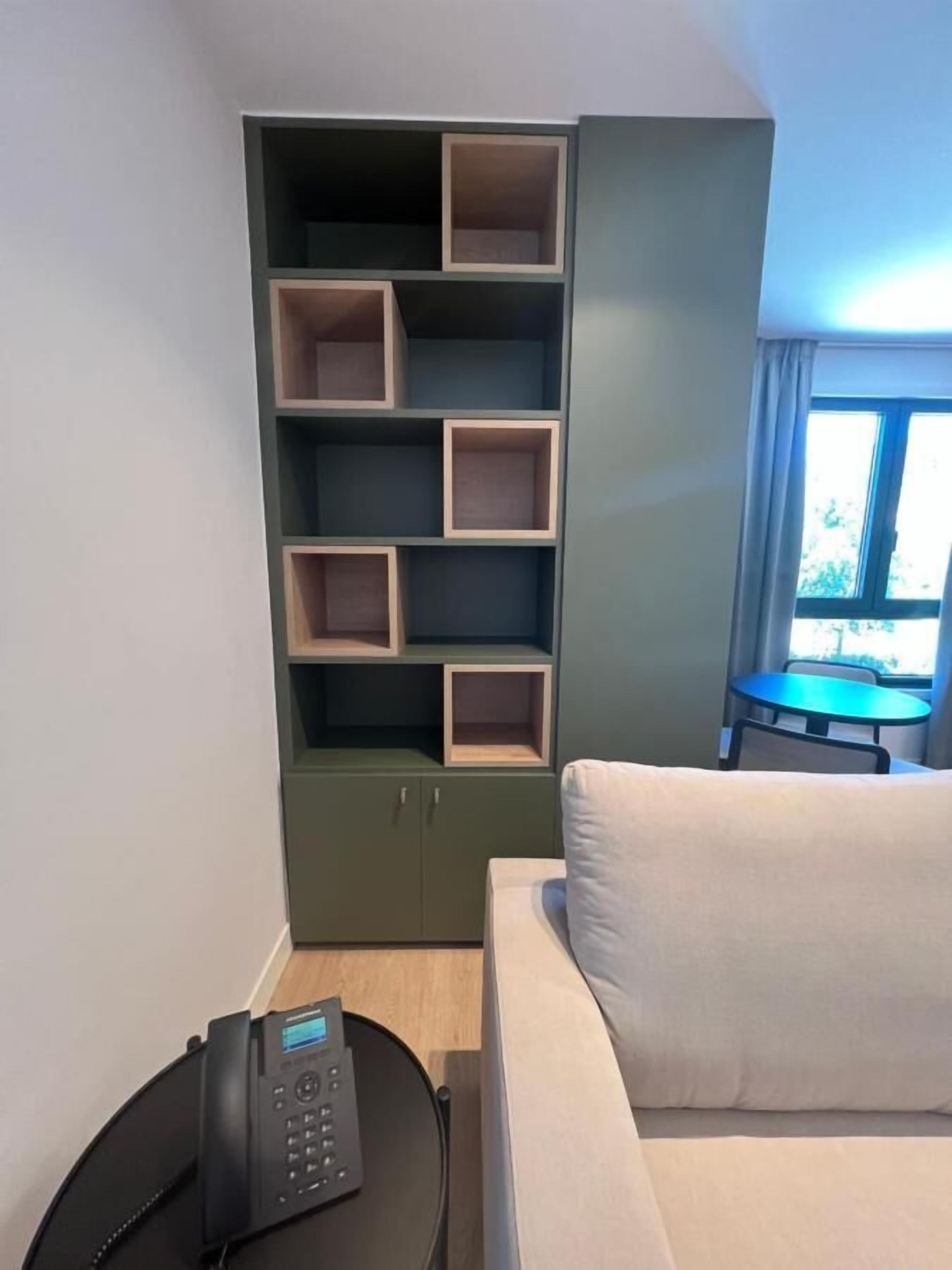 A hotel room with a green cabinet with multiple compartments, a white sofa, a small round table, and a telephone.