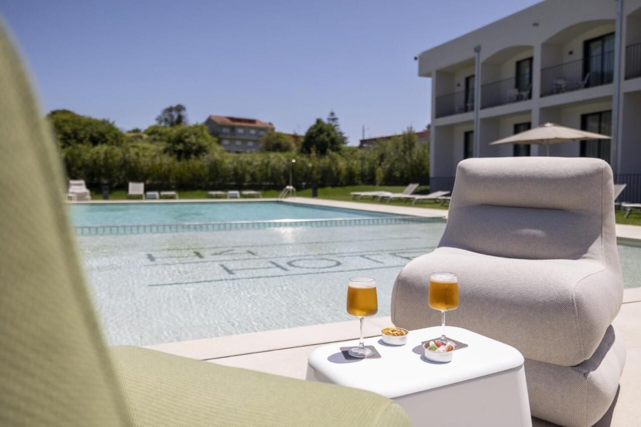 A poolside lounge with a white armchair, a small table with drinks, and a pool with a building in the background.