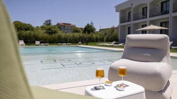 A poolside lounge with a white armchair, a small table with drinks, and a pool with a building in the background.