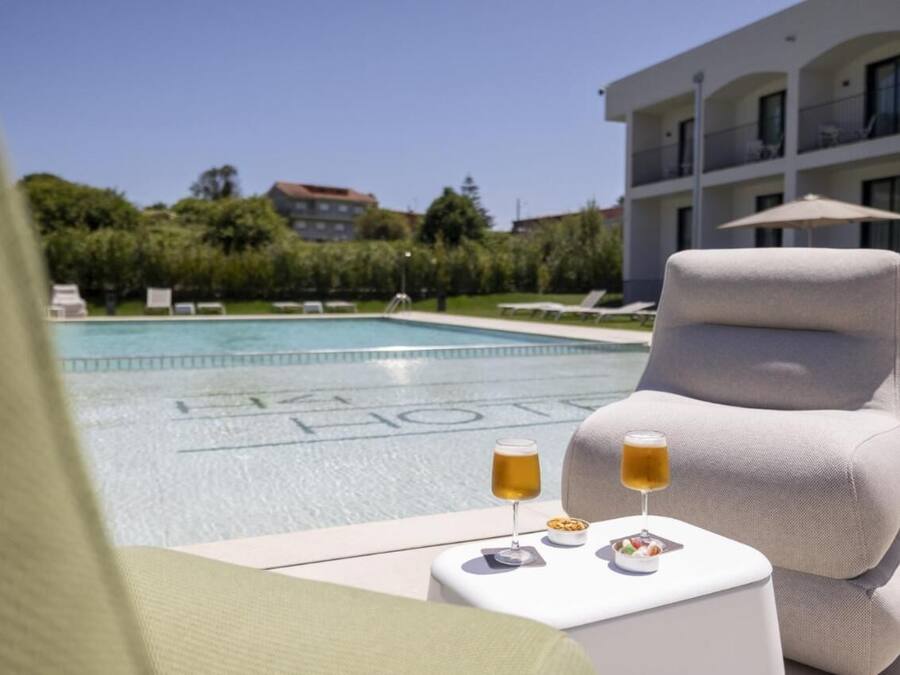 A poolside lounge with a white armchair, a small table with drinks, and a pool with a building in the background.