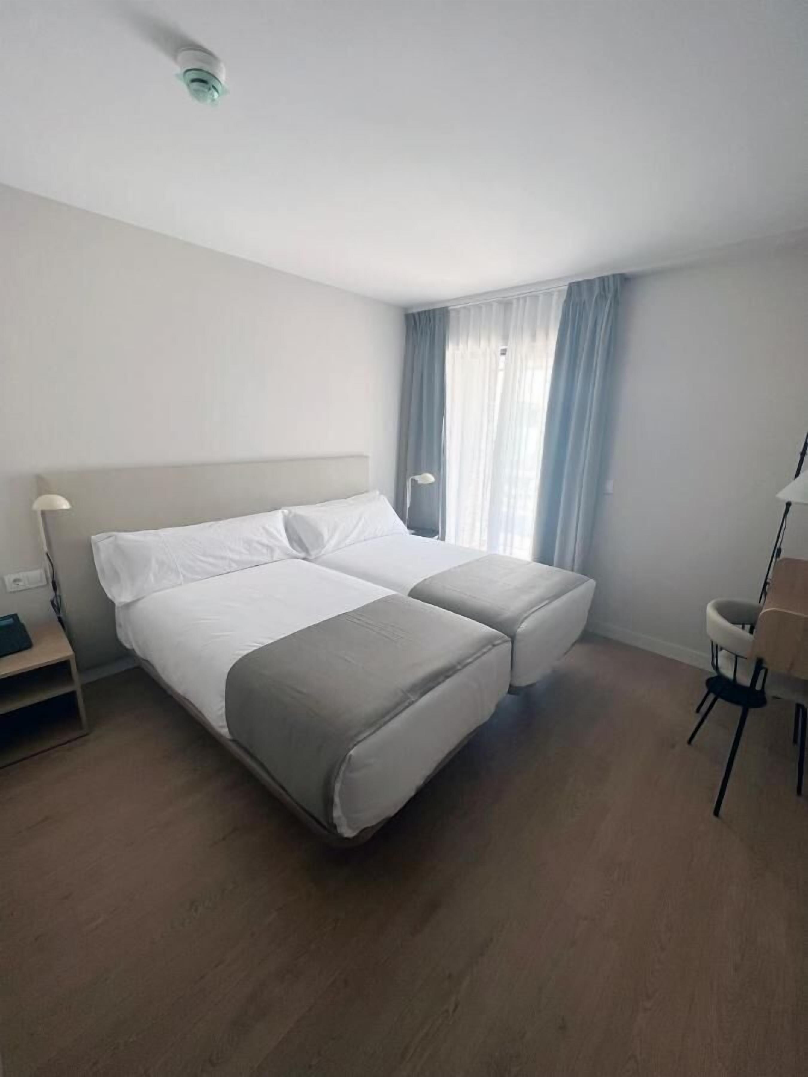A modern hotel room with a double bed, a desk, and a chair.