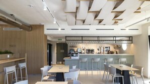 A modern cafe with a bar area, seating arrangements, and a visible menu board. - Hotel H4 Cangas (Cangas)
