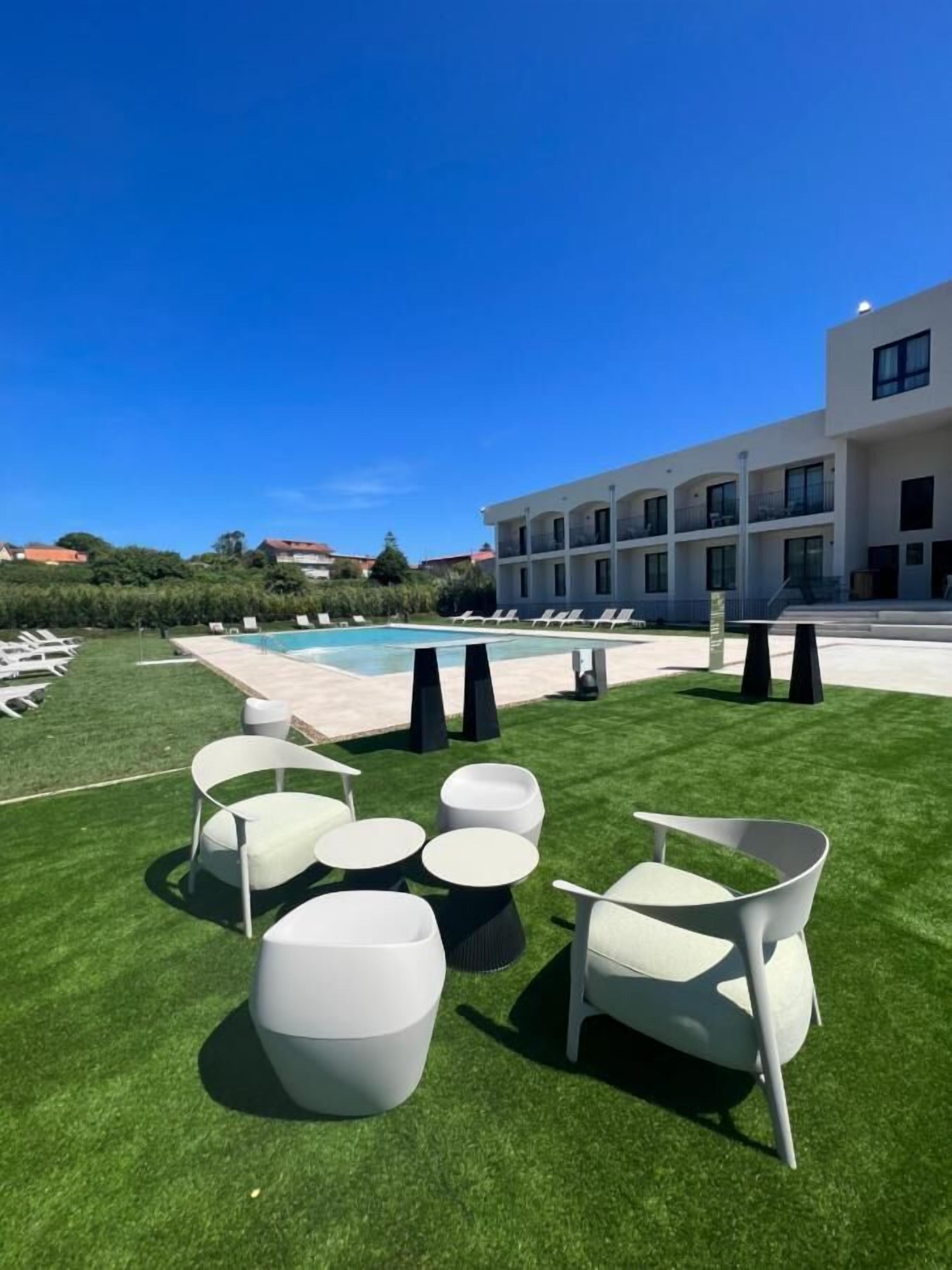 Zona de piscina exterior moderna amb gandules i taules blanques, cel blau clar i un edifici amb balcons al fons.