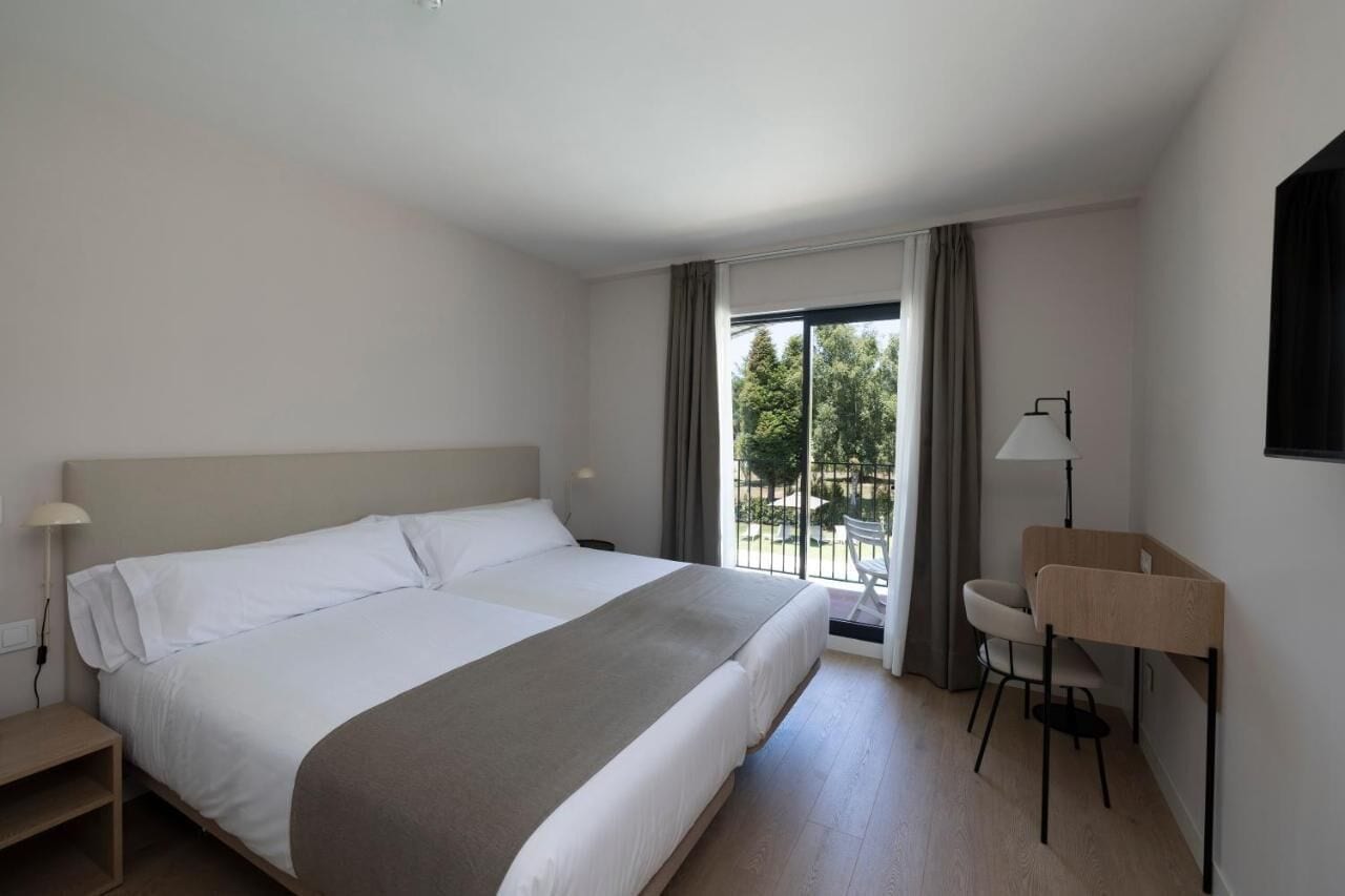 A hotel room with a large bed, a desk, a chair, and a view of the outdoors.