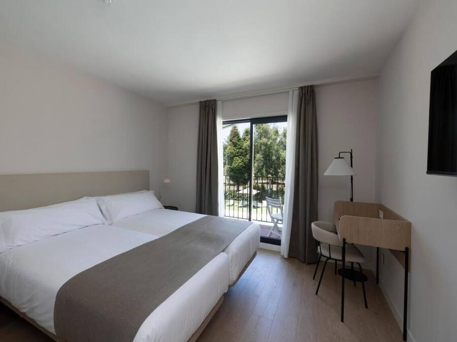 A hotel room with a large bed, a desk, a chair, and a view of the outdoors.