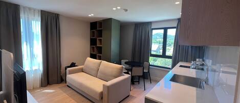 Una sala moderna con un sofá, una mesa de comedor con sillas, un televisor y una cocina con fregadero.