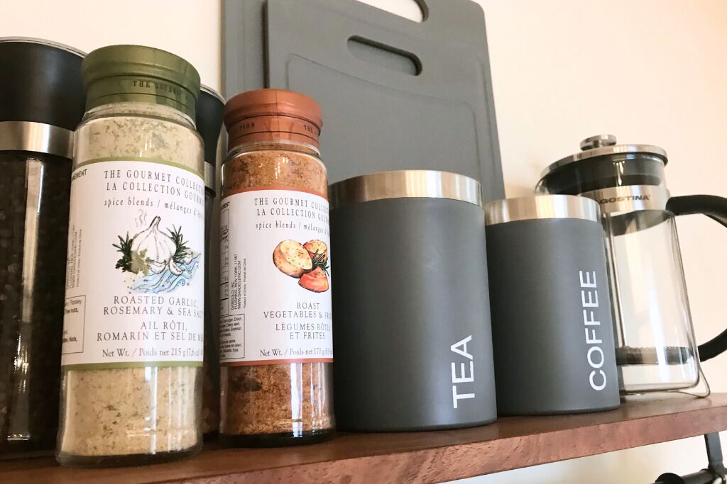 A shelf with various containers including labeled spice blends, a tea container, and a coffee container.