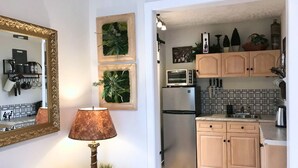 A compact kitchen with wooden cabinets, a stainless steel refrigerator, a microwave, and a toaster. There is a small countertop with a sink and a kettle.