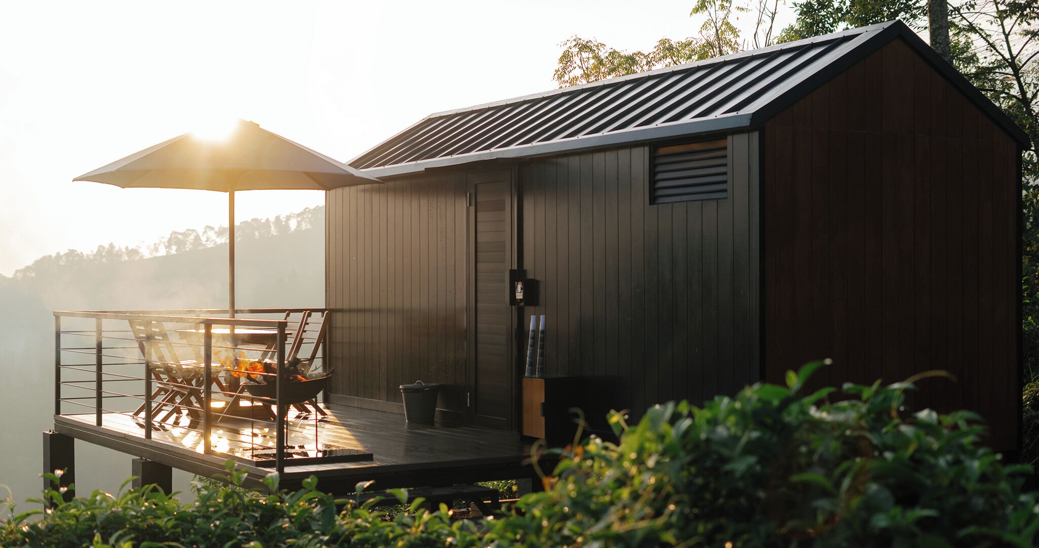 A wooden cabin with a deck and a table with chairs, overlooking a body of water.