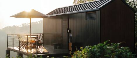 A wooden cabin with a deck and a table with chairs, overlooking a body of water.