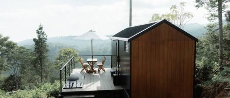 A wooden cabin with a deck, outdoor seating, and a view of the surrounding forest and hills.
