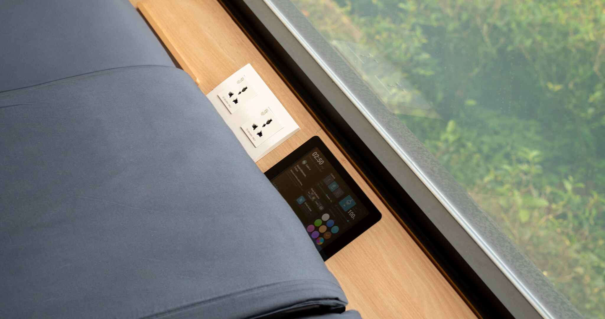 A bed with a grey sheet, a card with a QR code, and a digital clock displaying 02:50.
