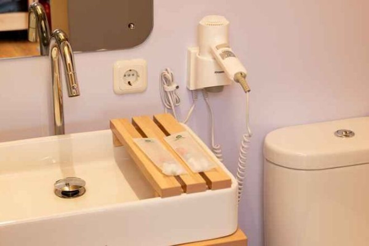 A bathroom with a white sink, wooden towel rack, and a hairdryer on a wall socket.