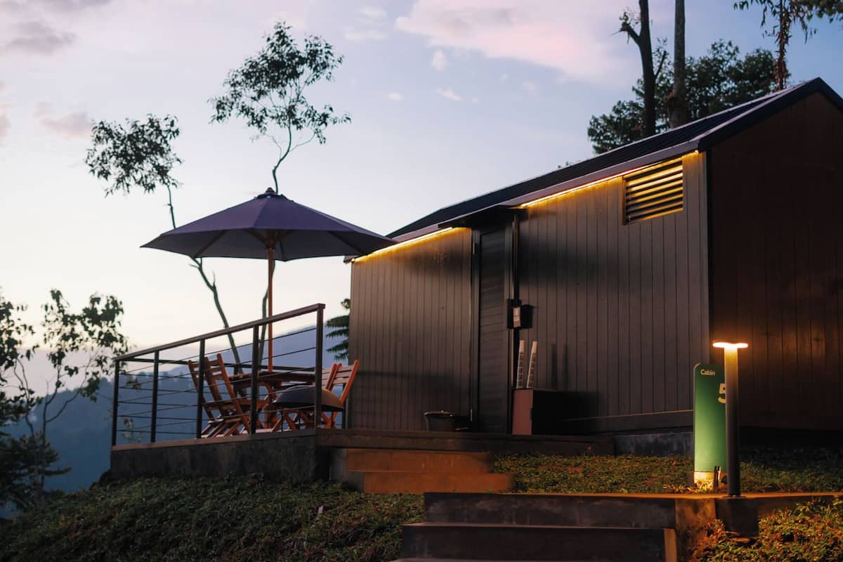A cabin with a wooden exterior, a porch with chairs, and a green sign indicating a cabin number.