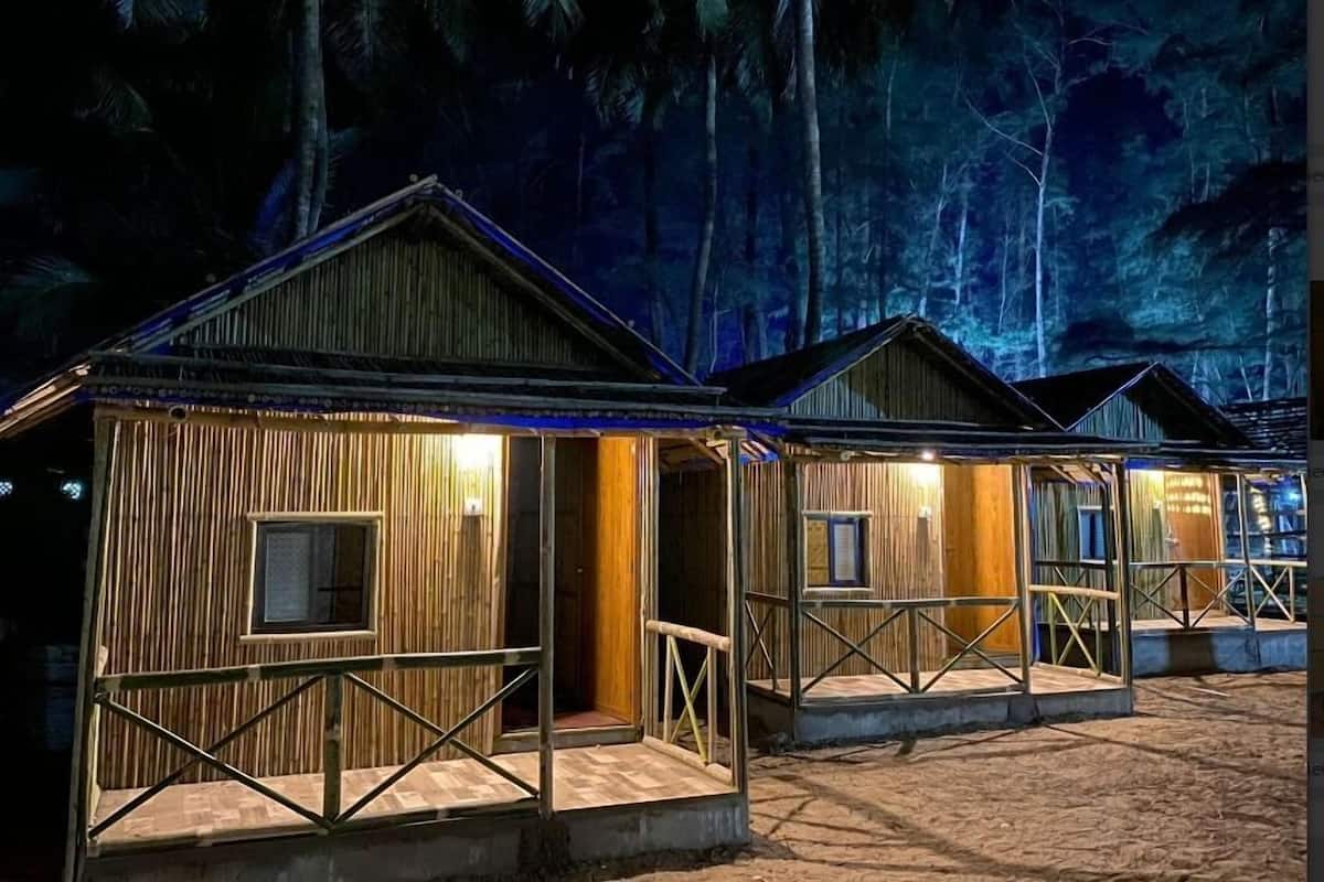 A row of wooden cabins with metal railings, set against a backdrop of dense foliage.