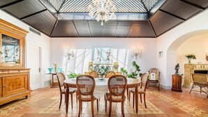 Un comedor con una mesa redonda, seis sillas de mimbre, una araña y una pared decorada con obras de arte enmarcadas.