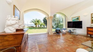 Un salón espacioso con televisor grande, un mueble de madera y vistas a un jardín a través de un arco.