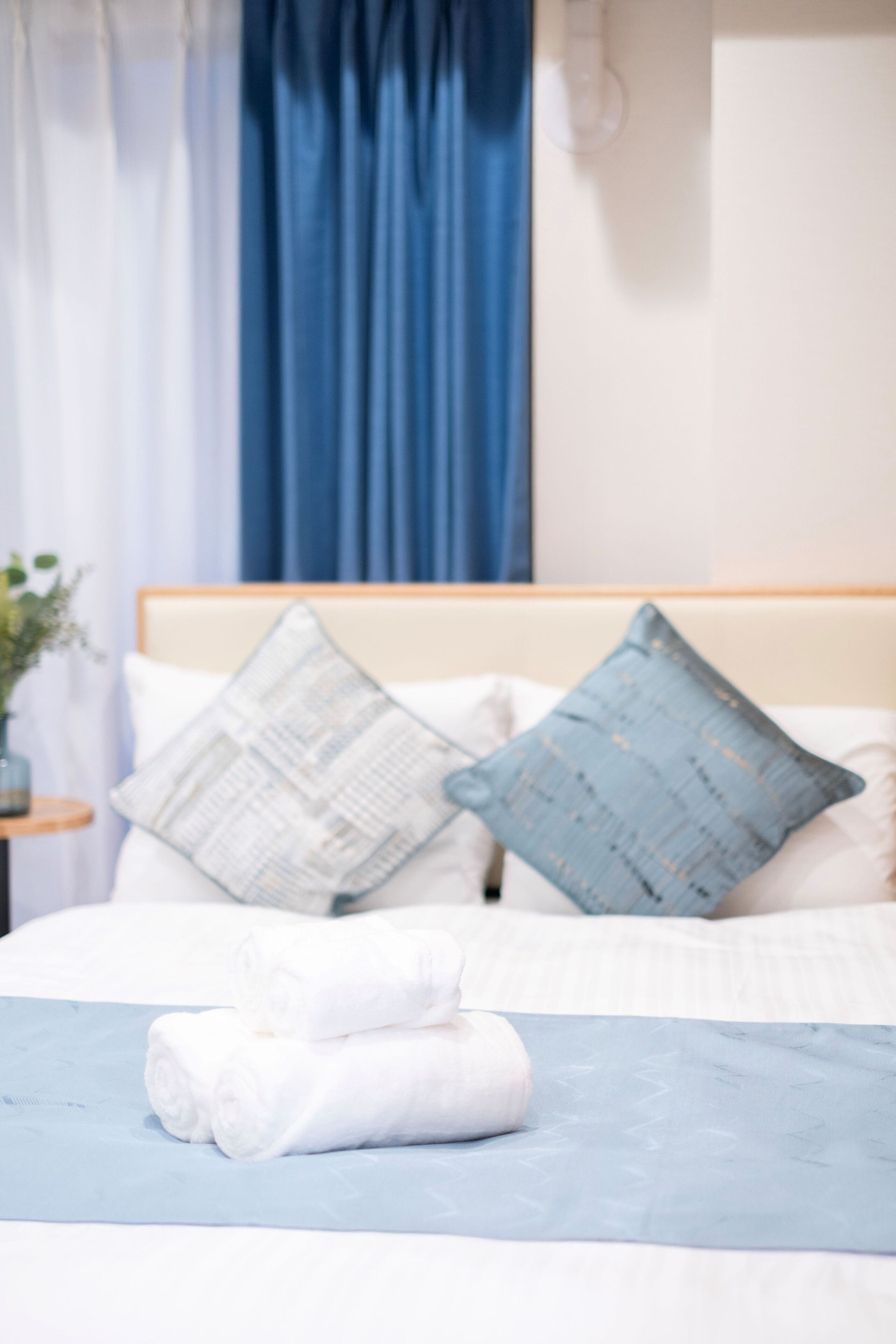 A neatly made bed with white and blue bedding, two pillows, and a folded towel.