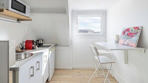 Una cocina compacta con microondas, hervidor y lavabo. Hay una ventana pequeña con vistas, y un cuadro en la pared.