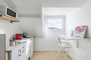 A compact kitchen with a microwave, kettle, and sink. There's a small window with a view, and a painting on the wall.