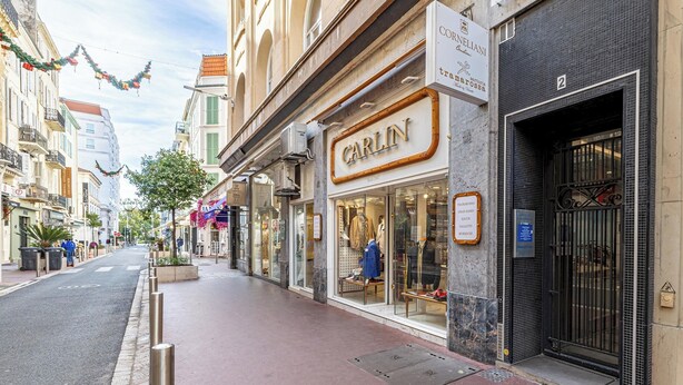 Vista de una calle con una fachada comercial que dice 'CARLIN' y un edificio con un cartel que dice 'CORNELIANI'.