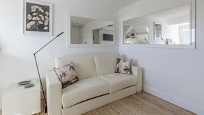 Una habitación con un sofá color beige, una mesita auxiliar, una lámpara de pie e impresión enmarcadas con motivos botánicos en la pared.