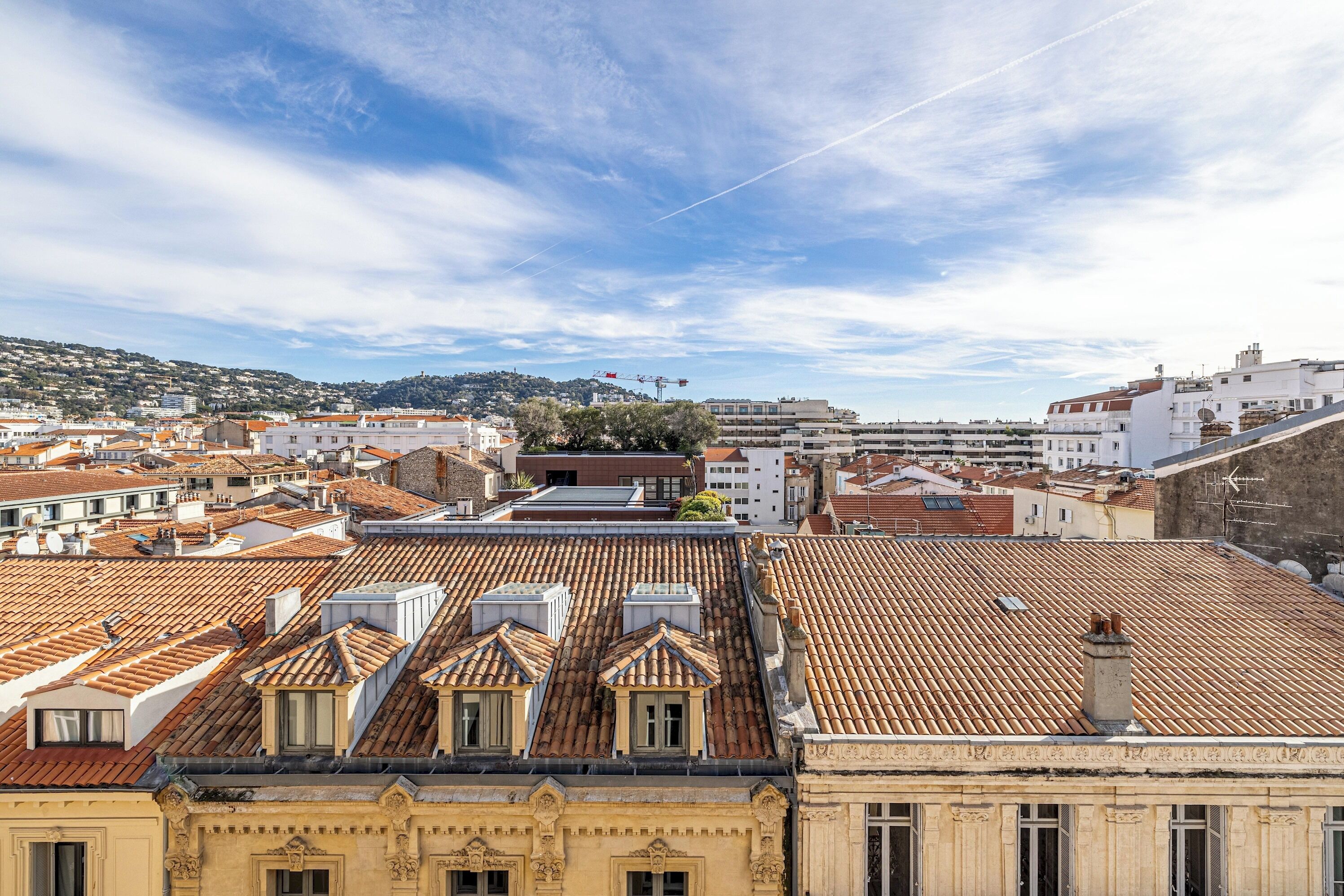 A cityscape with terracotta-tiled rooftops, a prominent building with ornate architecture, and a clear sky.