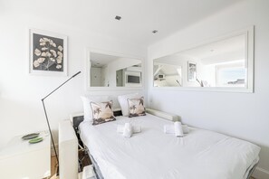 A hotel room with a bed, a large mirror, a framed botanical print, and a bedside lamp.