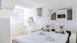 Un dormitorio con cama, almohadas, escritorio, silla, televisor y ventana.