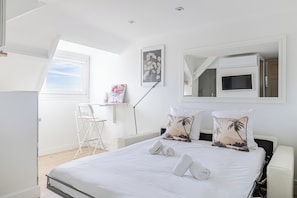A bedroom with a bed, pillows, a desk, a chair, a TV, and a window.