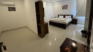 Una camera d'albergo moderna con un letto grande, un armadio in legno, una ventola a soffitto, un condizionatore d'aria e un piccolo tavolo con un oggetto decorativo.