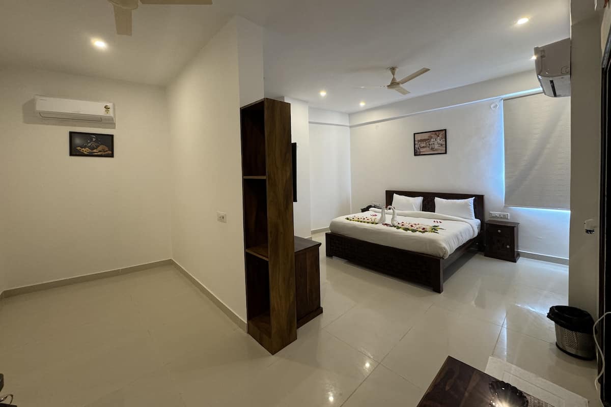 A modern bedroom with a large bed, two ceiling fans, an air conditioning unit, and a small bedside table.